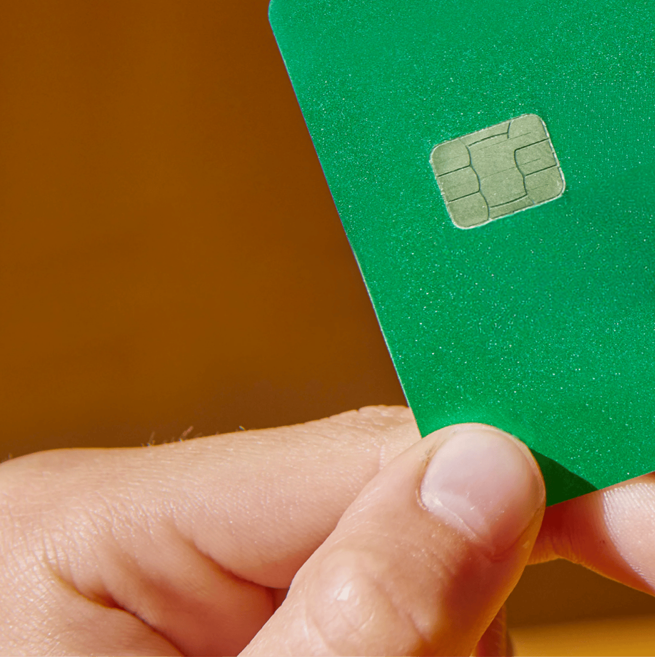 A hand holding a green card with a visible metallic chip.