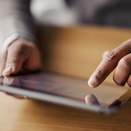 Close-up of hands using a tablet, a finger touching the screen.