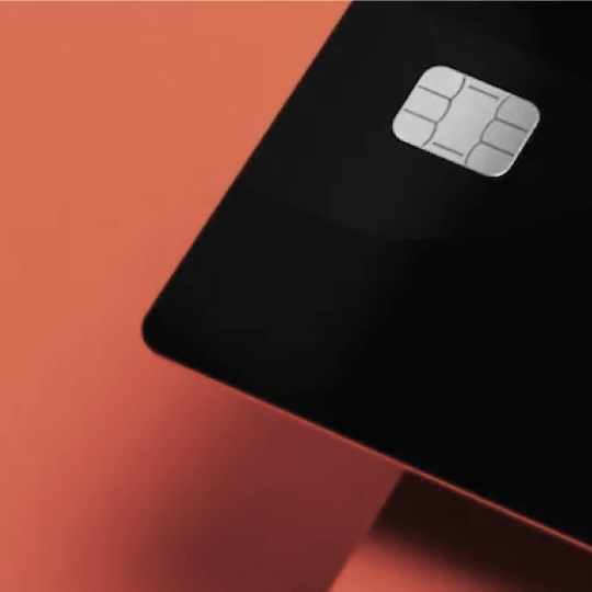Black credit card with a silver EMV chip on a reddish-orange surface.